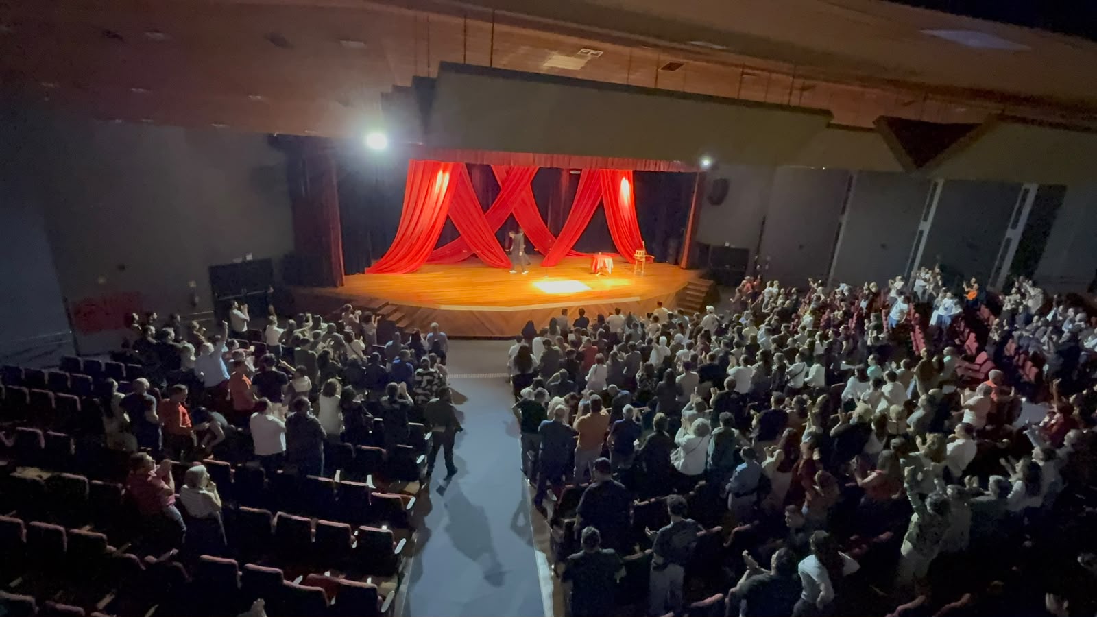 Visão ampla de uma apresentação, com palco e público de pé na plateia